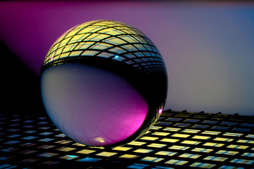 futuristic ball bearing reflecting purple and yellow neon lights sitting on a grid
